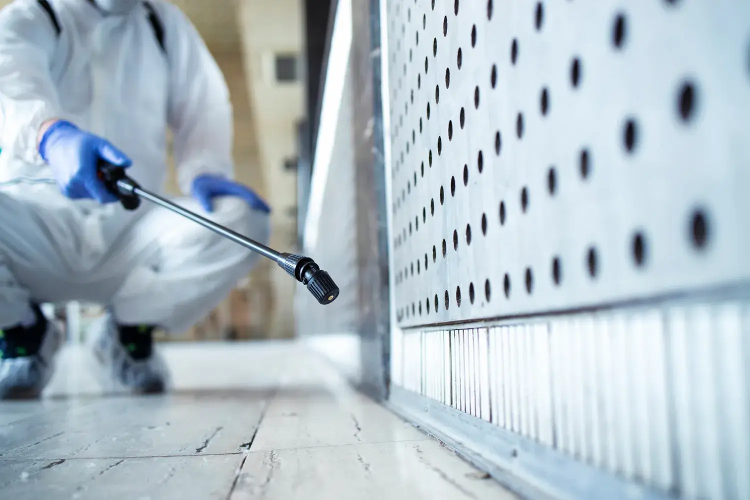 Pest control technician treating along an indoor wall vent